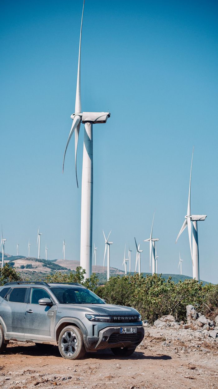 SUV parked near a wind farm under a clear blue sky, symbolizing adventure and renewable energy.