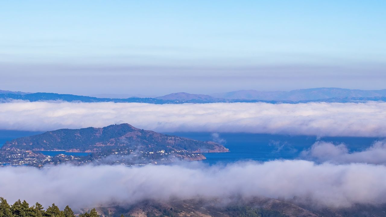 Stunning aerial view of fog enveloping San Francisco Bay with distant hills in the background.