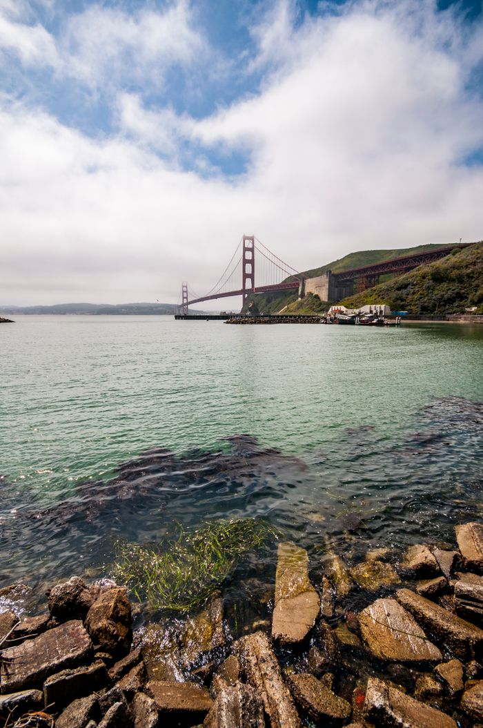 A picturesque view of the Golden Gate Bridge with serene water and rocky shoreline in San Francisco.